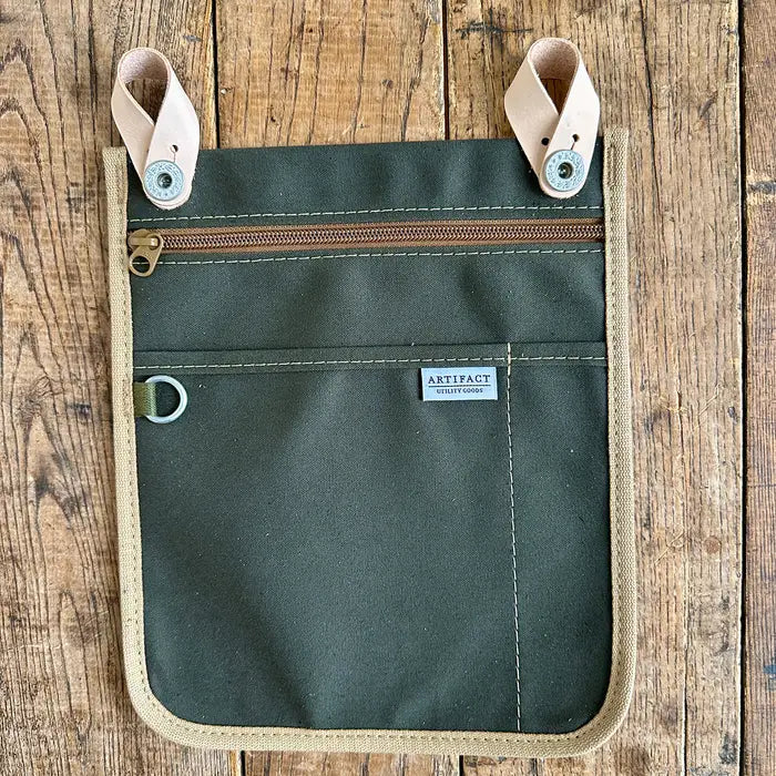 Green pouch with beige accents on a wooden surface, featuring the 'Artifact' brand label.