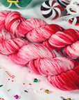 Two skeins of red and pink yarn on a white background with candy-themed decorations.