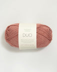 Ball of terra cotta colored yarn with a label on a white background