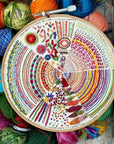 Embroidery hoop with colorful circular pattern surrounded by yarn and crochet hooks
