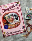 Embroidery kit with pink book cover and sample on a textured surface