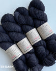 A collection of very dark purple mini skeins of yarn arranged together.