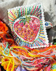 Colorful embroidered strawberry patch on fabric with colorful threads.