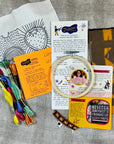 Embroidery kit with threads, hoop, and instructions on a textured fabric background