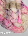 Multicolored skein of pink and purple speckles on a cream yarn with visible brand labels on a light gray background