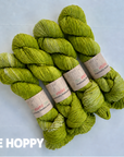 Four skeins of variegated yarn in a yellow-green shade labeled 'Best Buds' by EMMA'S YARN, arranged on a light gray background with the text 'BE HOPPY' in white at the bottom left.