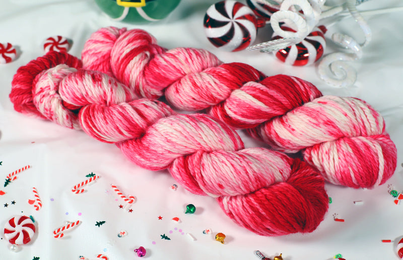 Two skeins of red and pink yarn on a white background with candy-themed decorations.