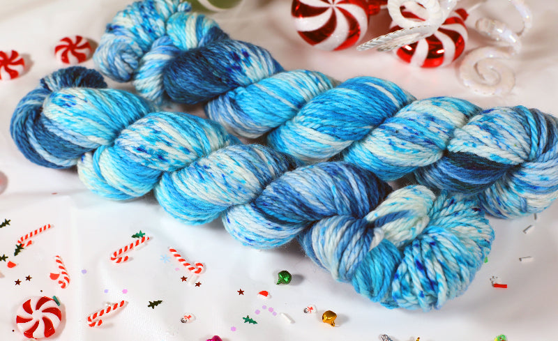 Blue and white yarn skeins on a festive background with candy canes and Christmas decorations.