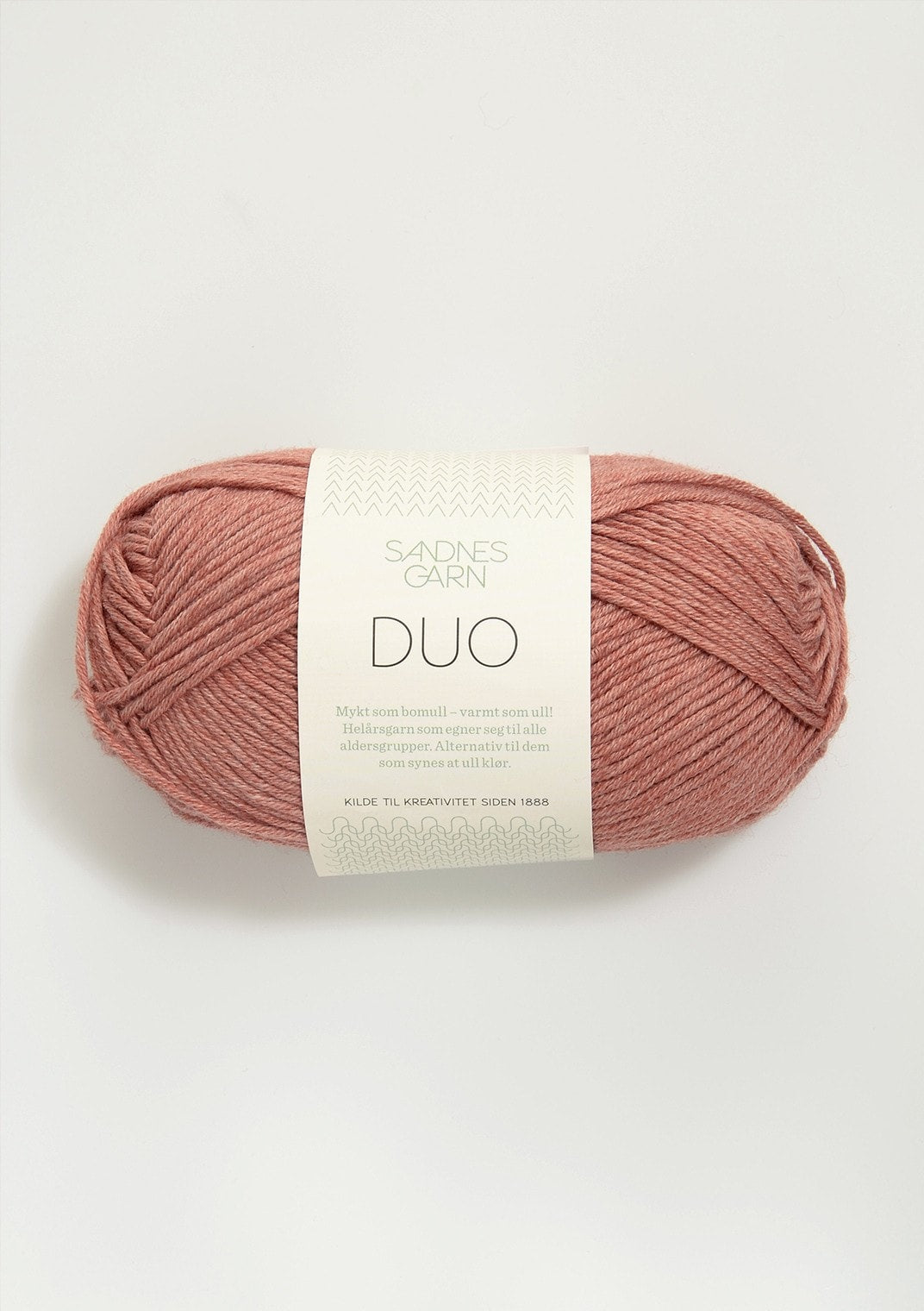 Ball of terra cotta colored yarn with a label on a white background