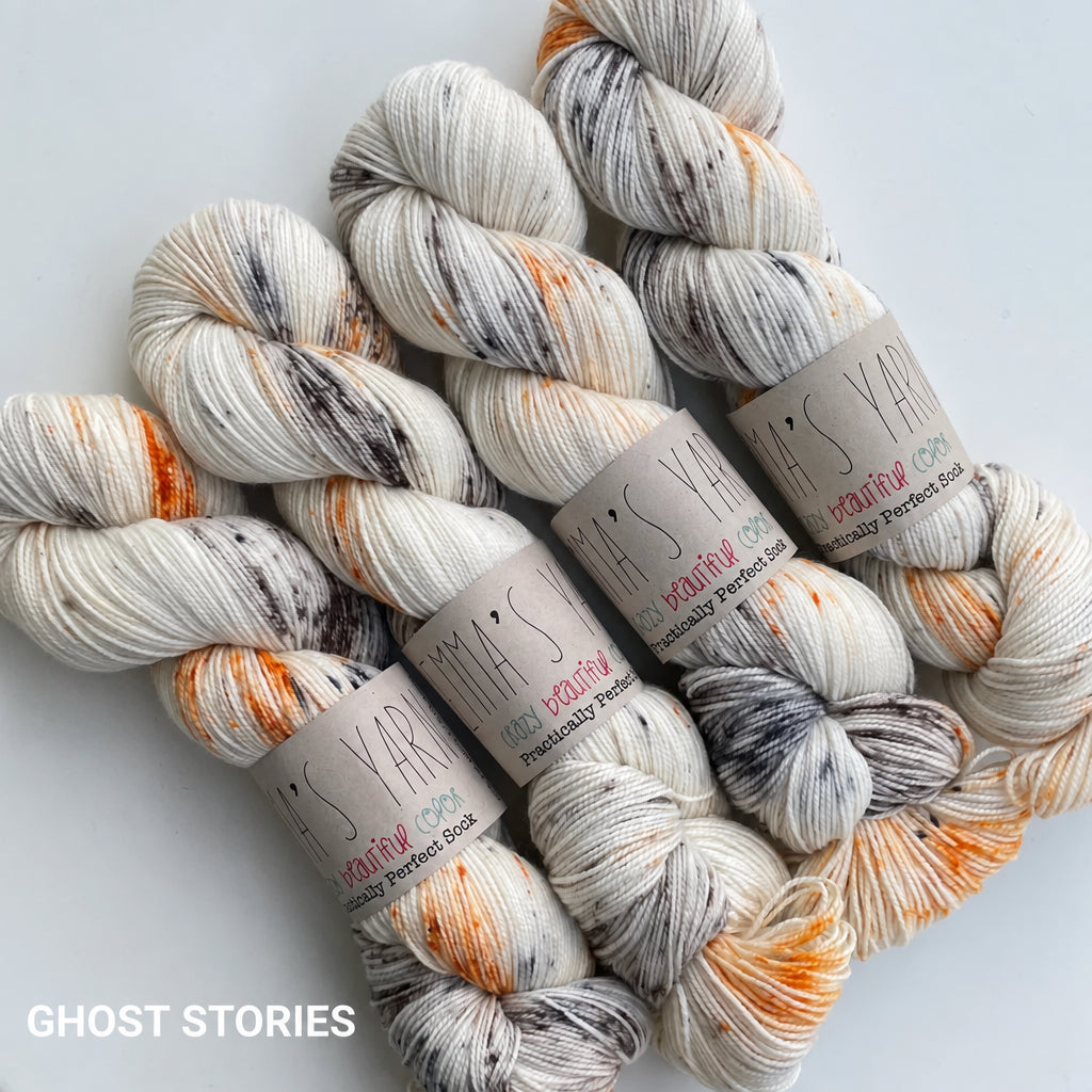 Four skeins of variegated yarn arranged on a light gray background. The yarn is primarily off-white/cream with orange, dark gray, and black variegated streaks.