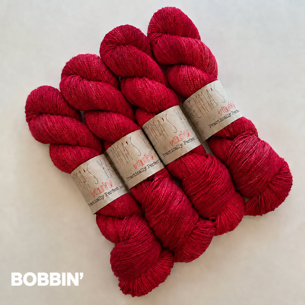 Three skeins of vibrant magenta-red yarn with paper bands, arranged on a light off-white background. The COLOR name 'BOBBIN'' .