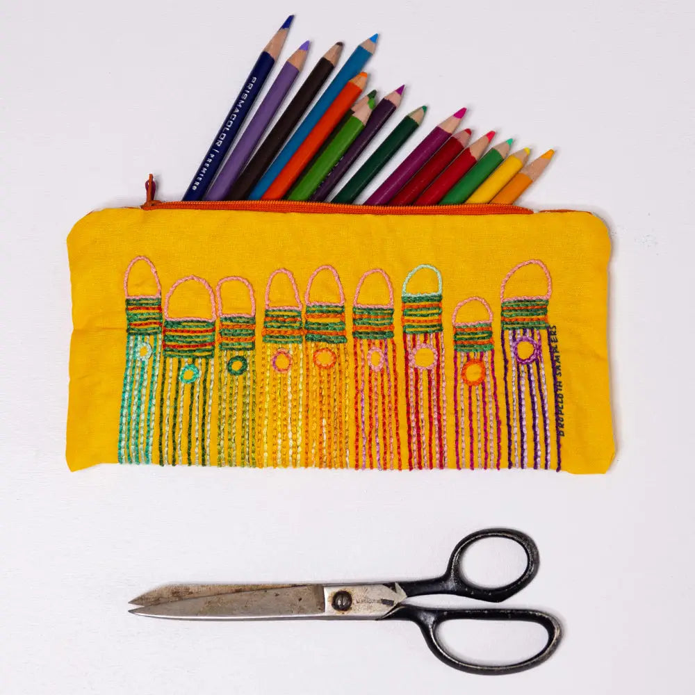 Yellow pencil case with colorful embroidered designs and pencils, accompanied by a pair of scissors on a white background.