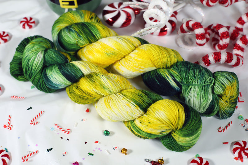 Two skeins of green and yellow yarn on a festive background with candy canes and Christmas decorations.