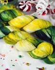 Two skeins of green and yellow yarn on a festive background with candy canes and Christmas decorations.