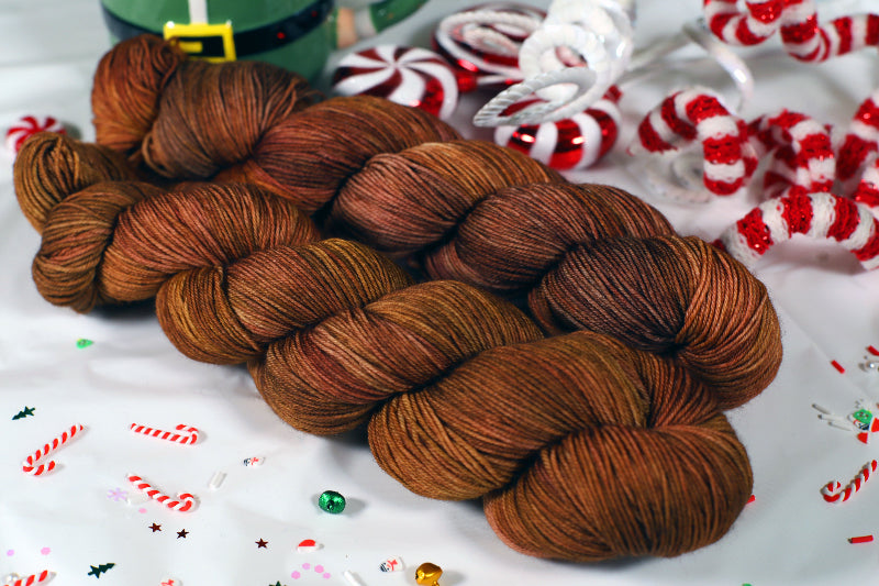 Brown yarn skein braided together with Christmas-themed decorations in the background