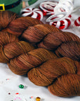 Brown yarn skein braided together with Christmas-themed decorations in the background