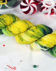 Two skeins of sparkly green and yellow yarn on a white background with Christmas-themed decorations.