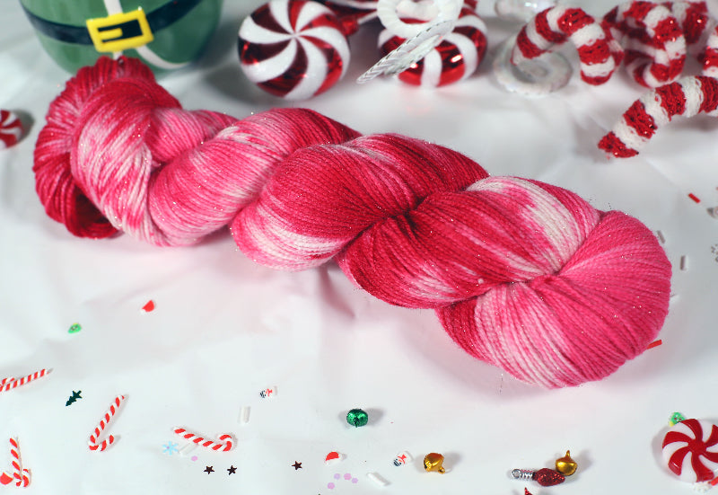 Pink, red and white sparkly yarn skein with Christmas-themed decorations on a white background