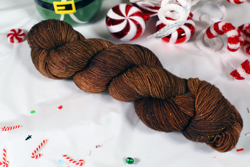 Brown skein of sparkly yarn on a white background with Christmas-themed decorations