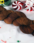 Brown skein of sparkly yarn on a white background with Christmas-themed decorations