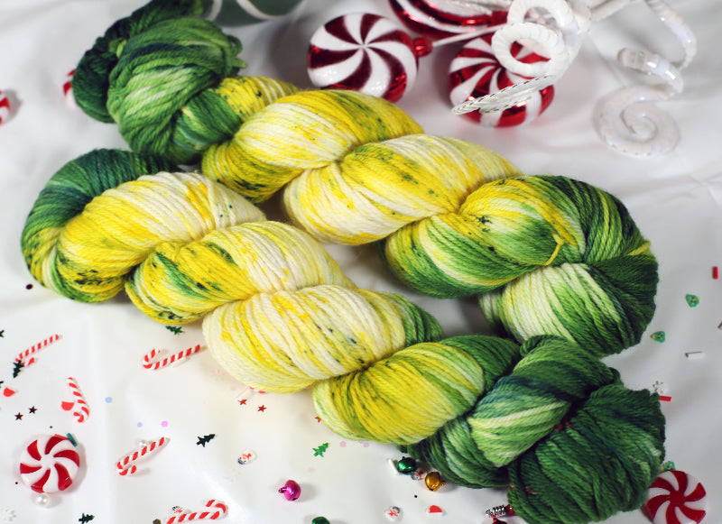 yarn skeins in green, yellow, and white on a festive background with candy canes and Christmas decorations.