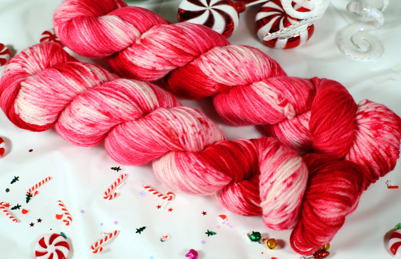 Red and pink yarn skeins on a festive background with candy canes and peppermints.