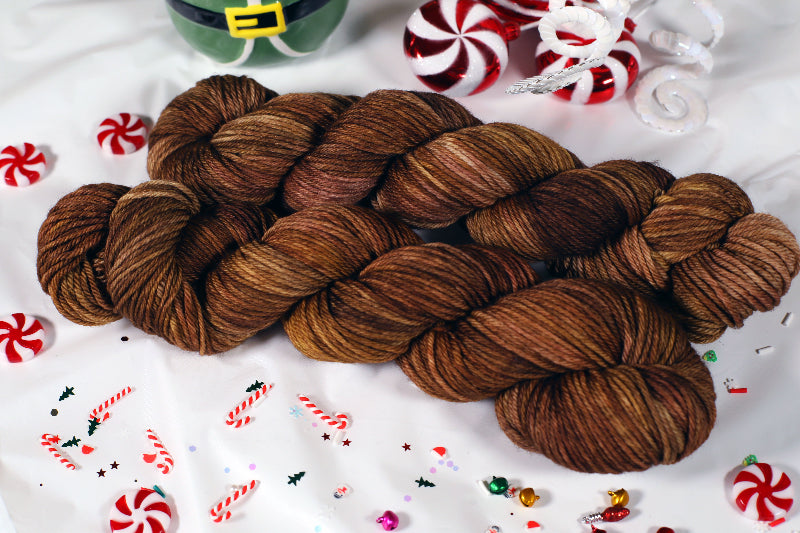 Two skeins of brown yarn on a white background with Christmas-themed decorations.