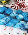 Blue and white skein of yarn on a festive background with candy canes and a gnome figurine.