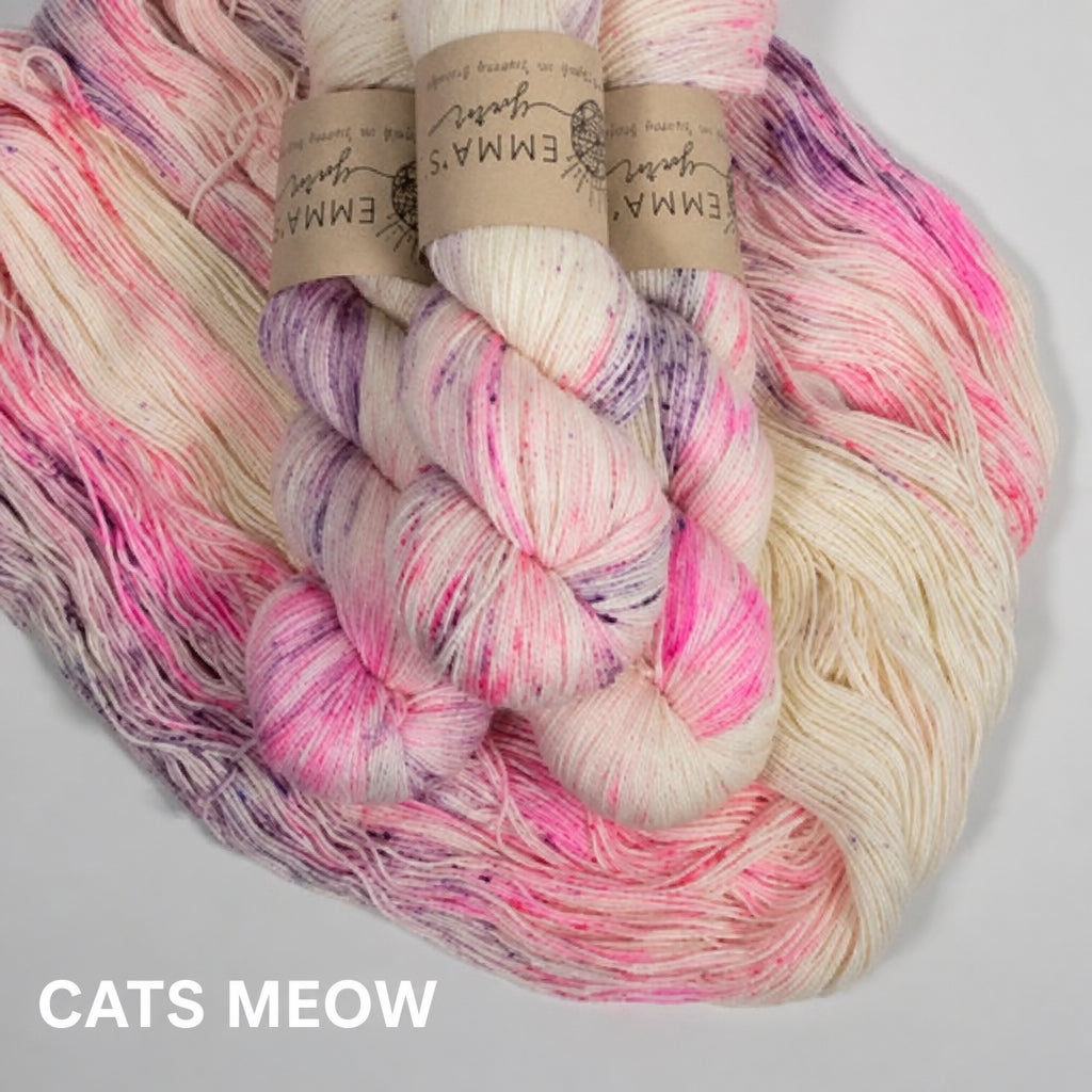 Multicolored skein of pink and purple speckles on a cream yarn with visible brand labels on a light gray background