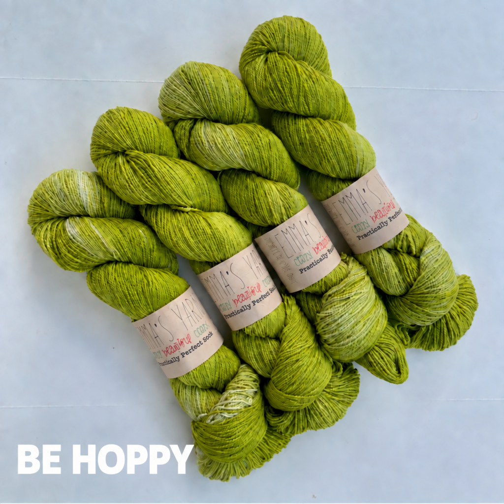 Four skeins of variegated yarn in a yellow-green shade labeled 'Best Buds' by EMMA'S YARN, arranged on a light gray background with the text 'BE HOPPY' in white at the bottom left.
